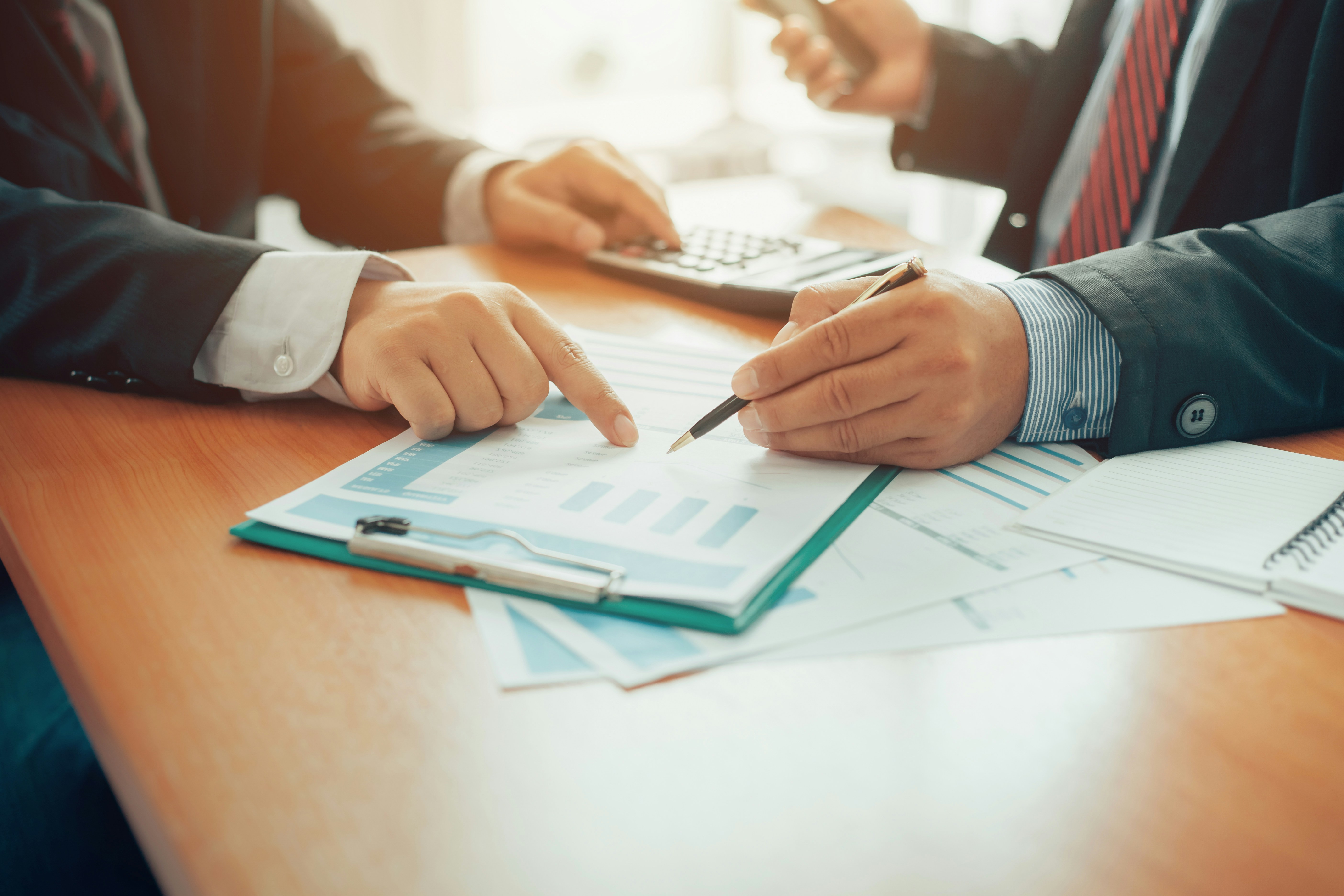 Two business professionals collaborate on paperwork at a desk, focused on their tasks and discussing details.