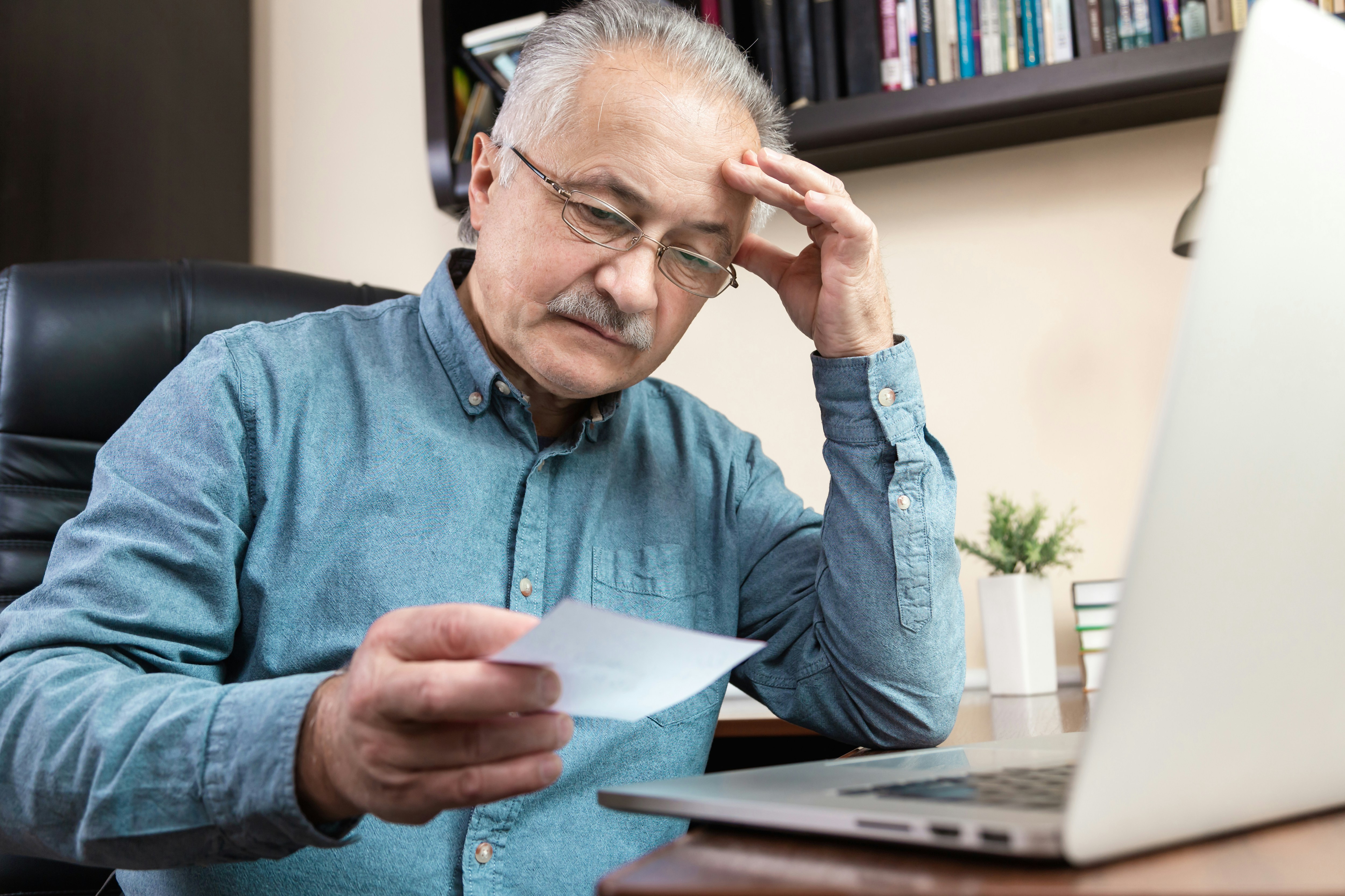 Senior man with glasses sitting at a desk, focused on his laptop while working.